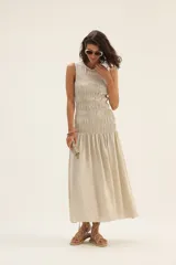 Vestido midi sin mangas confeccionado en lino color beige, con cuerpo superior ajustado mediante frunces elásticos y falda amplia con caída fluida.