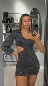 Minivestido negro con brillos plateados, de un solo hombro, manga larga y abertura en la cintura.