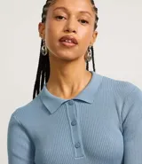 Vestido corto de corte evasé confeccionado en tejido de punto, con cuello polo, cierre frontal con botones y mangas largas.