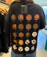 Remera oversize de algodón color negro con escote bote y costuras a la vista. Presenta una estampa en la espalda con múltiples diseños circulares que hacen referencia a balones de fútbol históricos.