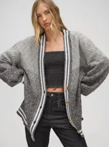 Cardigan de punto con diseño degradé en tonos grises, patrón tejido a rombos, corte oversize, cierre frontal con botones y detalles de rayas en los bordes y puños.