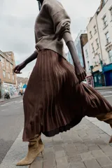 Falda midi plisada de tiro alto color marrón, con cinturón ancho de color beige y hebilla metálica cuadrada. Cierre lateral con cremallera oculta.