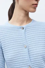 Chaqueta de punto color celeste, con cuello redondo, manga larga y cierre frontal con botones metálicos plateados.