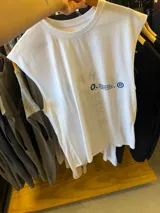 Musculosa blanca de corte holgado, sin mangas, con cuello redondo y un pequeño estampado azul en el pecho.