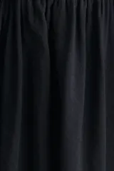 Vestido midi negro sin mangas, con cuello redondo y diseño ajustado en la parte superior de punto acanalado. Cuenta con una costura fruncida en diagonal bajo la cintura y una falda larga con vuelo de tejido fluido.