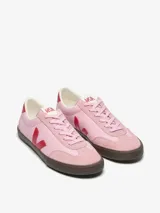 Championes Veja modelo Volley, de diseño inspirado en el voleibol de los años 70. Presentan una base de cuero en color rosa, con detalles en rojo en el logo lateral, talón y cordones. Cuentan con refuerzos de gamuza en la puntera y una suela de goma en color marrón oscuro.