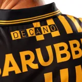 Camiseta de fútbol Puma del Club Atlético Peñarol, edición aniversario manga larga. Diseño con mitad derecha a rayas verticales amarillas y negras, y mitad izquierda negra con escudo retro "CUR" en dorado. Cuenta con cuello tipo polo negro con detalles amarillos y sponsors impresos en el frente y mangas.