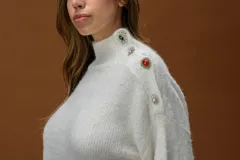 Polera de punto color blanco, de corte relajado y cuello alto. Presenta detalle de botones joya decorativos en uno de los hombros.