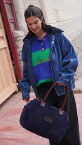 Bolso amplio de gamuza azul con manijas largas de cuero marrón. Cuenta con bolsillos laterales, uno con clip, cierre posterior y un bolsillo interno amplio. Presenta detalle de bandera y logo bordado en los laterales.