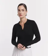 Blusa de punto ajustada color negro, con cuello polo y escote pronunciado en V. Presenta un tejido acanalado vertical en el torso y mangas largas.