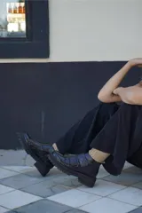 Borcego de cuero color marrón oscuro con acabado desgastado en la puntera. Presenta un diseño de caña corta con cierre lateral y dos tiras ajustables con velcro en el empeine. Cuenta con una suela de goma robusta tipo tractor.