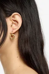 Caravanas de doble aro entrelazados en tono dorado. Un aro está decorado con cristales de colores incrustados en el borde exterior y el otro presenta el logo de la marca grabado. Cuentan con cierre de gancho.