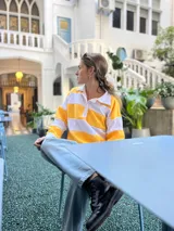 Sweater de punto a rayas horizontales amarillas y blancas, con cuello polo y mangas largas.