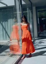 Vestido midi de color naranja con diseño estilo globo, confeccionado en tejido de algodón. Presenta un cuerpo ajustado tipo palabra de honor con tirantes finos y una falda con bajo abullonado.