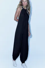 Mono largo de lyocell color negro, con cuello halter, cierre lateral con cremallera oculta y botones en el cuello. Presenta un diseño holgado con bajo acabado en puño elástico.