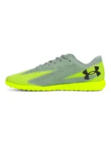 Championes de fútbol Under Armour Shadow Select 3 Turf, diseñados para césped artificial. Presentan un empeine sintético suave y resistente en color gris con detalles en amarillo neón, incluyendo el logo de la marca en negro. Cuentan con suela de goma con tacos multidireccionales para un agarre óptimo.