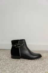 Botas cortas de cuero negro con paneles traseros de gamuza, cierre lateral y detalle de correa con hebilla metálica en el tobillo.