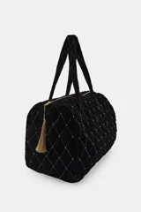 Bolso tipo shopper acolchado confeccionado en terciopelo negro. Presenta un diseño de rombos con hilo metalizado y aplicaciones de brillos en las intersecciones. Cuenta con doble asa de hombro, cierre superior con cremallera y detalle de pompón decorativo en el tirador.