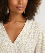 Blusa color crema con estampado animal print de jaguar en tonos dorados, escote en V, mangas 3/4 y nudo en la parte inferior.