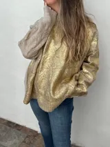 Buzo de tejido de punto grueso color beige con mangas largas y detalles dorados en el cuerpo.