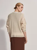 Cárdigan color crema de tejido de punto calado, con cuello redondo, cierre frontal con botones y corte holgado.