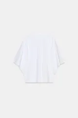 Camiseta blanca de manga corta con corte oversize y cuello redondo. Presenta un diseño de manga tipo capa que cae holgadamente desde el hombro.