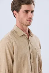 Camisa de lino de manga larga en color beige, con cuello camisero, cierre frontal de botones y un bolsillo ojal en el pecho.