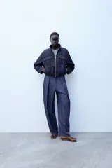 Cazadora bomber de denim oscuro con cuello subido, manga larga y bolsillos frontales con solapa. Presenta cierre frontal de cremallera y bajo elástico.