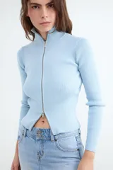 Sweater de punto celeste con diseño acanalado, cuello alto y cierre frontal con doble cremallera metálica, de manga larga y calce al cuerpo.