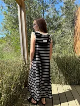 Vestido largo de punto a rayas horizontales negras y blancas, sin mangas, con cuello redondo y volados blancos en cuello y sisas.