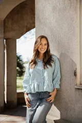 Camisa de algodón a rayas verticales en color verde y blanco, con cuello camisero, mangas largas y un detalle de volado en el ruedo que le otorga una silueta acampanada.