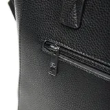 Cartera tipo tote bag de cuero sintético negro con textura granulada. Cuenta con doble asa superior, correa ajustable extraíble, bolsillo frontal con cierre metálico y logo de la marca grabado en la parte inferior.