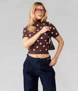 Sweater de punto color chocolate con estampado de lunares rosados, cuello alto y mangas cortas. Presenta un calce ajustado al cuerpo con terminaciones acanaladas en cuello, mangas y ruedo.