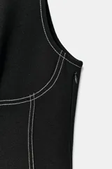 Vestido mini negro con cuello redondo y diseño sin mangas, con pespuntes en contraste y botones decorativos frontales.