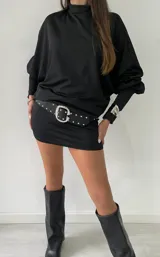 Vestido corto negro de cuello alto, con mangas largas abullonadas y puños ajustados. El diseño presenta un corte entallado en la falda y un estilo minimalista.