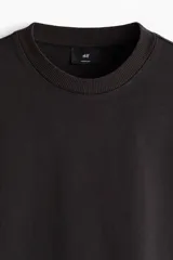 Remera boxy de algodón en punto liviano, de color negro, con hombros caídos, cuello redondo acanalado y corte oversized.