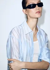 Camisa oversize de manga larga a rayas celestes y blancas, con cuello solapa camisero y cierre frontal de botones.