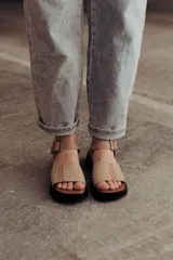 Sandalia de cuero color tostado con tiras anchas, tira en el talón y hebilla metálica rectangular ajustable. Cuenta con suela de goma con tacón bajo y plataforma.