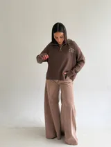 Sweater de tejido bremer color blanco, con cuello polo, cierre frontal y bordado en el pecho. Presenta mangas largas y diseño de corte holgado con terminaciones acanaladas.