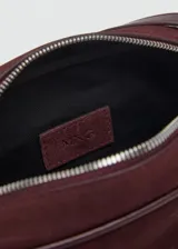 Bolso bandolera de tamaño pequeño confeccionado en piel de serraje color bordó, con cierre de cremallera y asa larga ajustable.