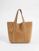 Cartera tipo shopper de gran tamaño confeccionada en material efecto gamuza color rojo. Presenta correas reforzadas decoradas con tachas metálicas plateadas y un dije colgante en forma de corazón con detalles de tachas. Cuenta con una placa metálica pequeña con logo en la parte inferior frontal.