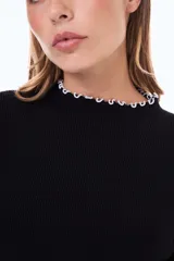 Buzo de tejido de punto acanalado en color beige, con cuello alto y terminaciones con borde ondulado en contraste negro en cuello y puños.