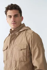 Campera de gabardina color beige con capucha desmontable y ajustable, cierre frontal con cremallera y bolsillos tipo cartera.