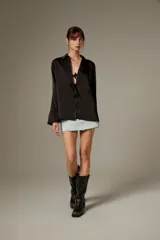 Blusa negra de poliéster, con cuello camisero, mangas largas y cierre frontal mediante tiras para anudar.