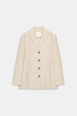 Blazer de Zara Woman Collection confeccionado en mezcla de lino, color beige con diseño de rayas verticales sutiles. Cuenta con cuello solapa, manga larga, bolsillos de parche en el frente y cierre frontal con botones oscuros a contraste.