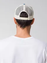 Gorro tipo trucker de color azul denim en la parte frontal y visera, con malla trasera blanca. Presenta un estampado frontal con la inscripción "Caterpillar" y la silueta de un vaquero montando un caballo. Incluye cierre trasero ajustable.