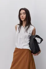 Blusa sin mangas color negro, de silueta fluida, con cuello redondo, detalle de alforzas en el frente y abotonadura parcial con botones visibles.