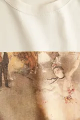 Remera oversized de punto de algodón color crema, con cuello redondo acanalado y hombros caídos. Presenta un estampado frontal de la obra "L'Étoile" de Edgar Degas y texto alusivo.