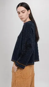 Sweater de lana color beige con calce holgado y cuello redondo. Presenta un bordado negro con diseño de arabescos en una de las mangas y detalles de rayas y puntos en contraste en el ruedo y los puños.