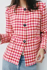 Blazer corto de tweed con estampado a cuadros en tonos rojo, rosado y blanco, cuello redondo, manga larga y cierre frontal con botones negros.
